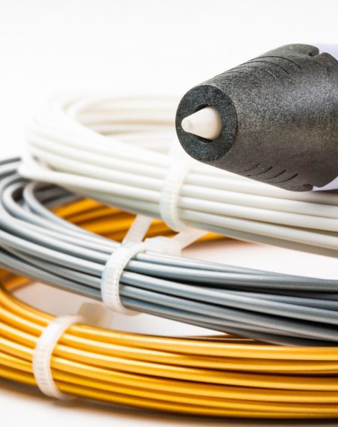 Closeup view of bunch of colorful rolled cables and childrens 3D printing pen isolated on white. Three bright filament plastic lying indoors. Concept children's entertainment and creativity.