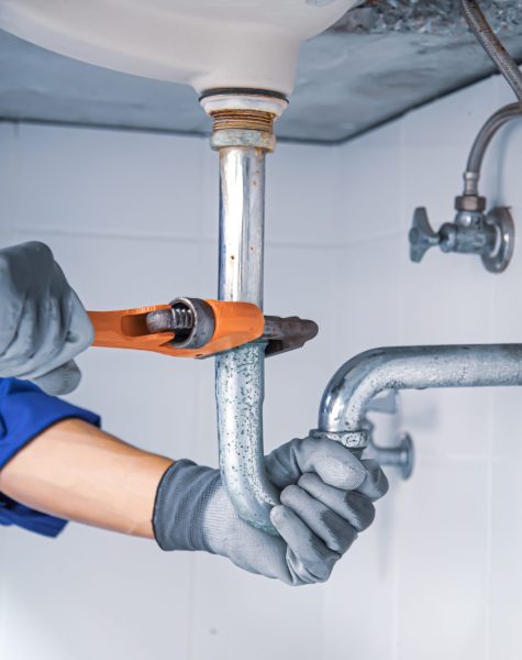 Technician plumber using a wrench to repair a water pipe under the sink